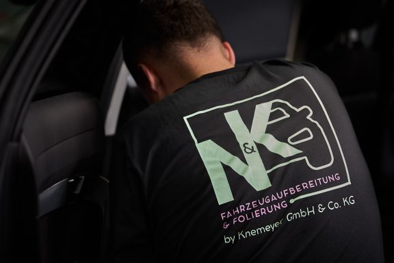 Person mit T-Shirt von NK-Automobilveredelung, arbeitet an einem Auto.