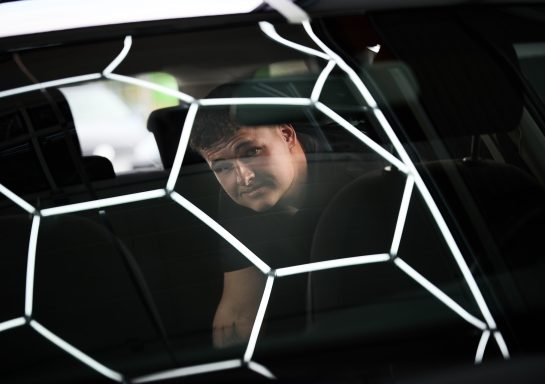 Ein Mann sitzt im Auto hinter einem Netz mit sechseckigen Mustern.